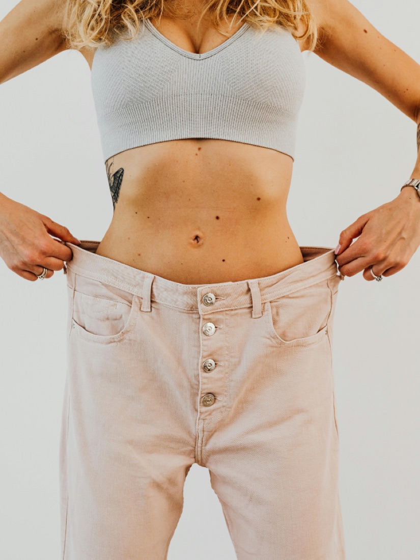 Woman holding out the waistband of her old jeans after losing weight